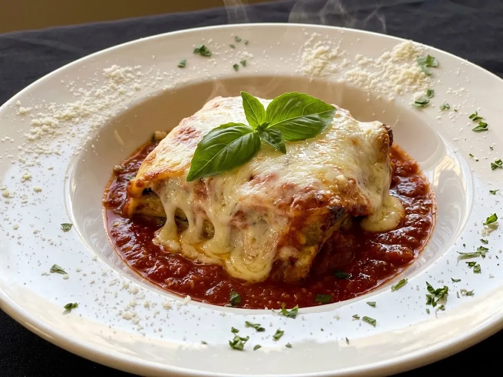 A square of lasagna under melted mozzarella and fresh basil, in a pool of red sauce